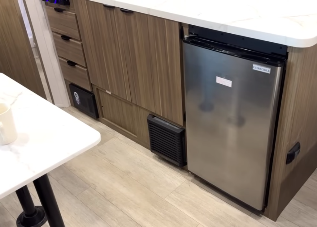 Forest River Wildwood FSX RV kitchen lower cabinetry with Everchill 12V refrigerator, wood panel drawers, and modern light flooring for a clean, compact layout.