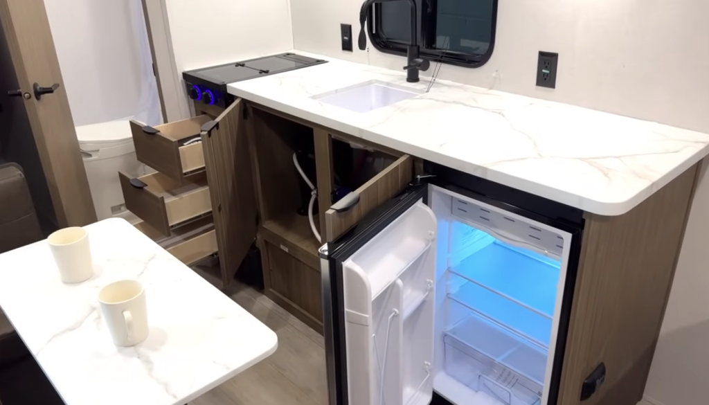 Under-sink cabinet in the Forest River Wildwood FSX revealing plumbing lines, water pump, and PEX tubing beneath the RV’s kitchen counter.