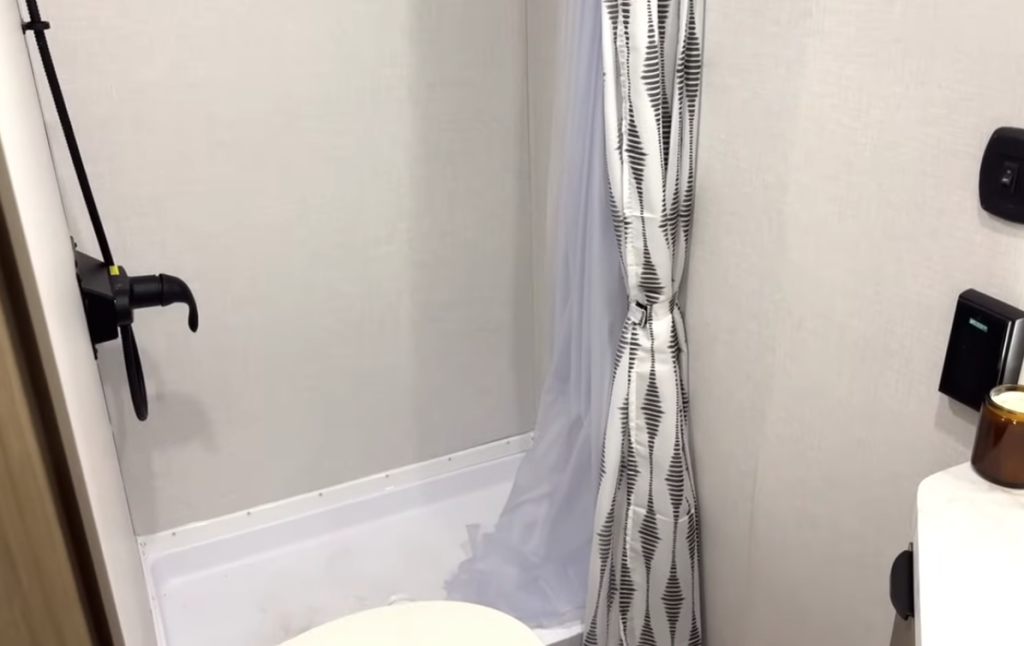 Forest River Wildwood FSX RV bathroom with shower-tub combo, black faucet, patterned curtain, and compact layout for lightweight trailers.