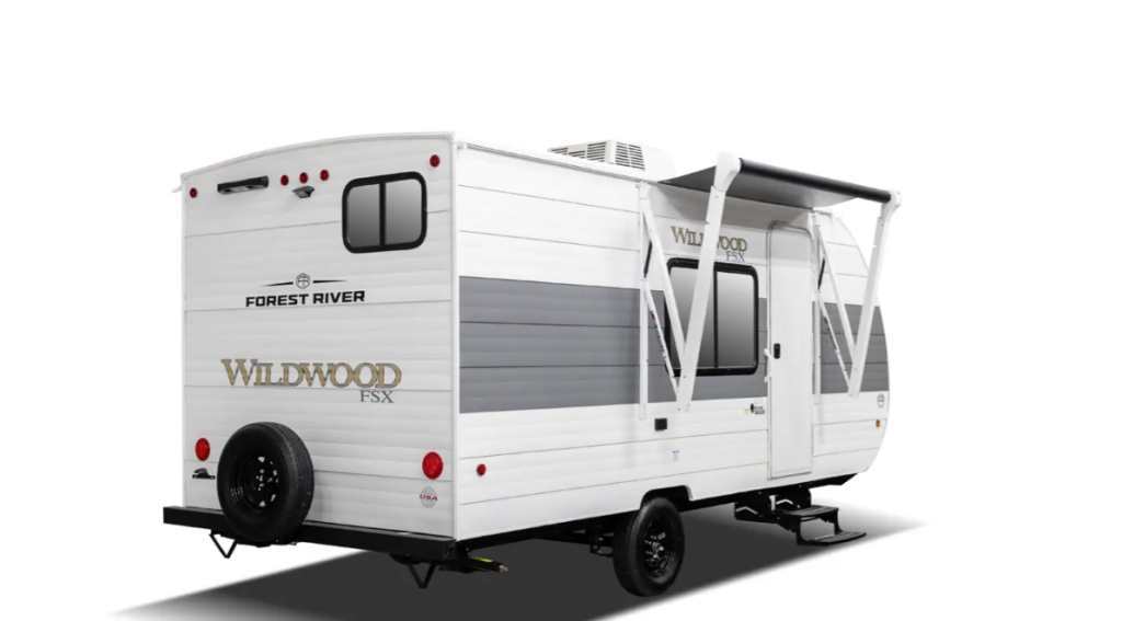 Forest River Wildwood FSX lightweight travel trailer with single axle, rear spare tire, entry steps, and extended awning for outdoor shade.