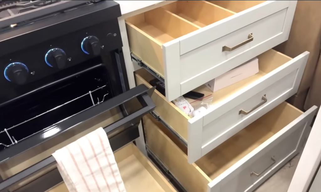 Brinkley Model Z fifth wheel kitchen drawers open beside black oven with blue LED knobs, showcasing organized storage, soft-close drawers, and luxury RV kitchen cabinetry.