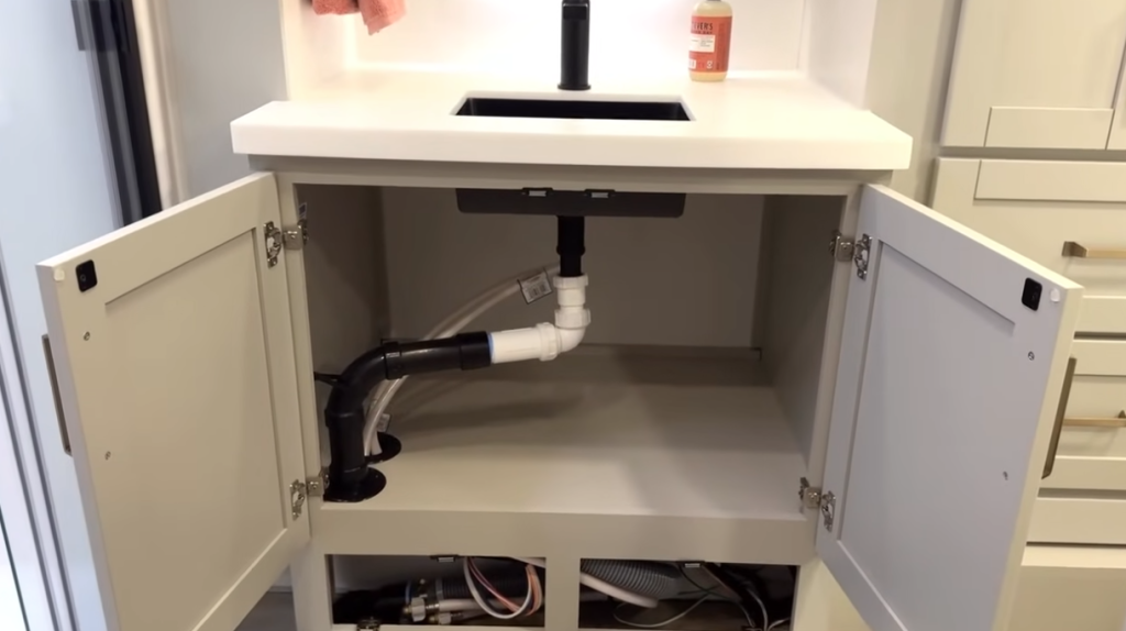 Brinkley Model Z RV bathroom vanity with both cabinet doors open, revealing accessible under-sink plumbing and storage space ideal for toiletries or cleaning supplies, designed for easy maintenance.