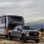 Ford Super Duty truck towing a Brinkley Model Z fifth wheel RV through a scenic mountain landscape at sunset, showcasing premium design, luxury construction, and off-road towing capability.