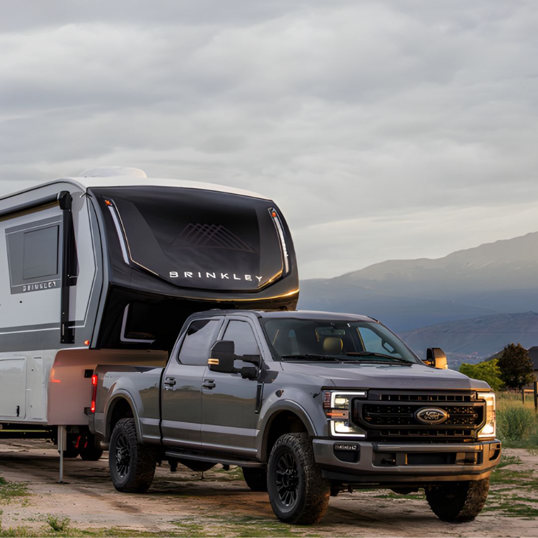 Ford Super Duty truck towing a Brinkley Model Z fifth wheel RV through a scenic mountain landscape at sunset, showcasing premium design, luxury construction, and off-road towing capability.