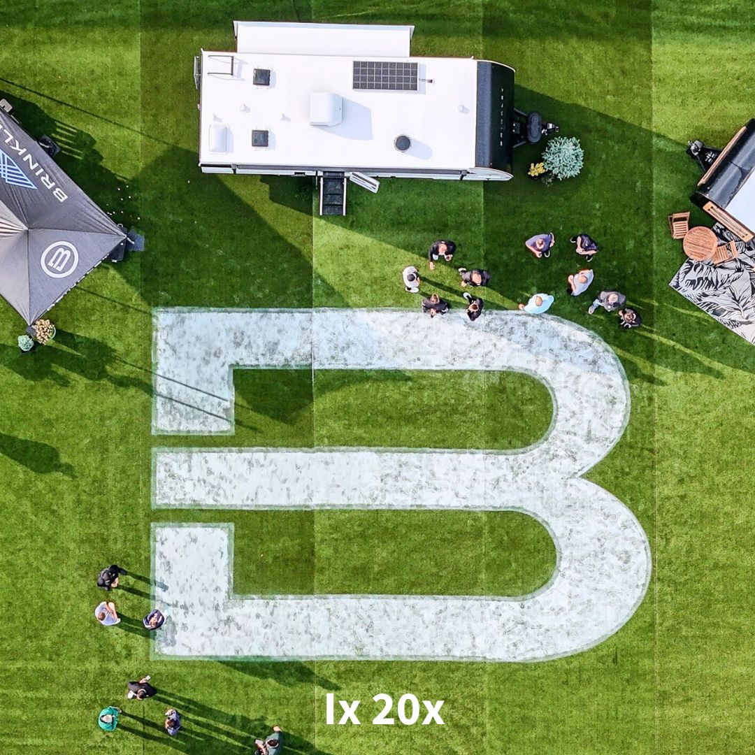 Aerial view of Brinkley RV outdoor event featuring the Model IX 20X, large Brinkley “B” logo on grass, and attendees exploring the travel trailer display.
