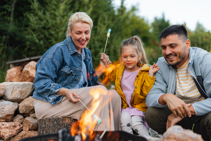 A family of three gathers around a campfire, roasting marshmallows and enjoying a delightful outdoor moment. The scene captures warmth, happiness, and togetherness in a natural setting.