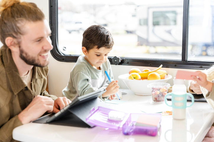 Boy uses a tablet while his father works; fruit bowl in background.
