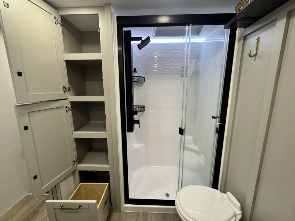 Brinkley Model Z 3600 bathroom with large walk-in shower, porcelain toilet, and open storage cabinets showcasing spacious shelving and a pull-out drawer for organized storage.