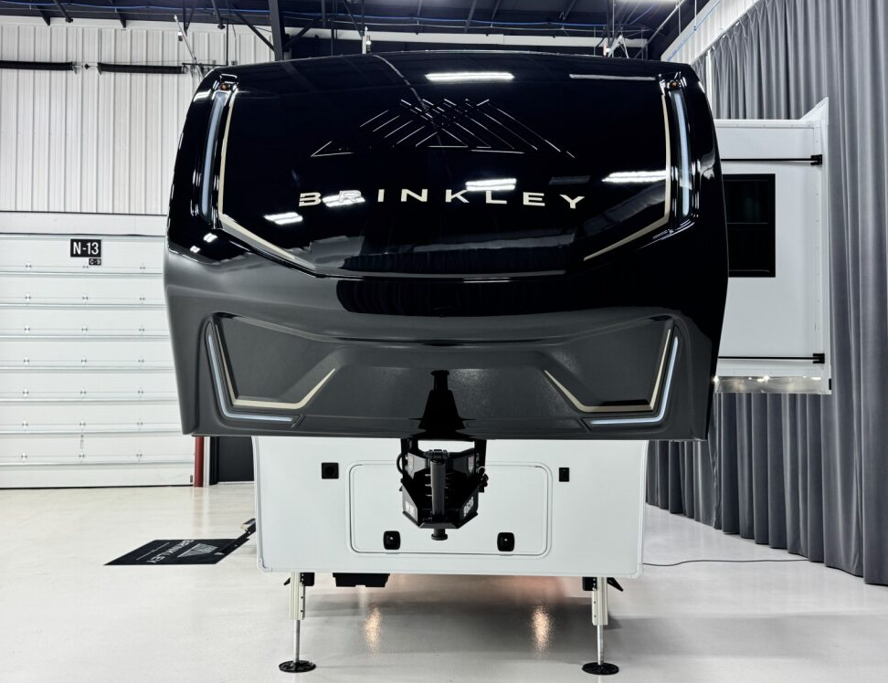 Front view of the Brinkley Model Z fifth wheel RV showing its sleek black aerodynamic front cap with bold Brinkley logo and modern LED accent lighting inside a display showroom.