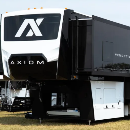 Front exterior of the 2026 Axiom Vendetta fifth wheel toy hauler showcasing its bold black-and-white design, aerodynamic front cap with Axiom logo, high-gloss steel-laminated sidewalls, and spacious pass-through storage area, representing luxury construction and modern RV engineering.