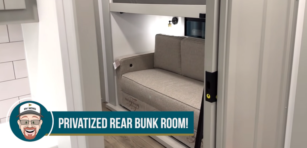 RV rear bunk room with a privatized sliding door, lower sofa bed, upper bunk, modern lighting, and light gray upholstery, shown with RV Nerd graphic overlay.