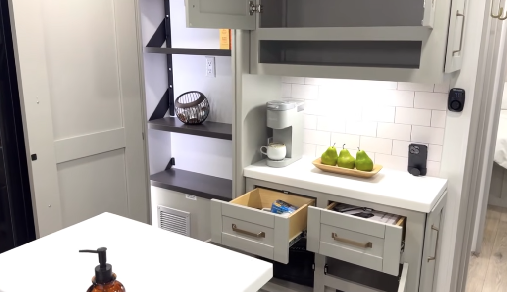 RV kitchen coffee bar area in the 2026 Brinkley Model Z Air featuring subway tile backsplash, open shelving, a Keurig coffee maker, decorative pears, and multiple soft-close drawers open below the counter.