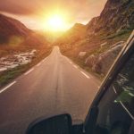 Sunset view from an RV window on a scenic mountain highway—empty two-lane road with river and rocky slopes glowing in golden light, ideal for road-trip travel.