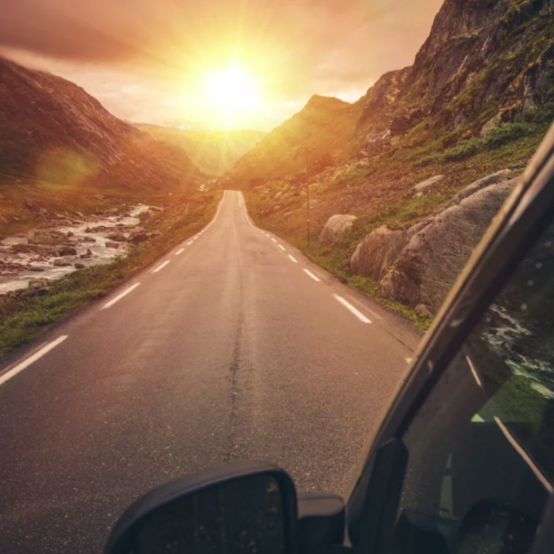 Sunset view from an RV window on a scenic mountain highway—empty two-lane road with river and rocky slopes glowing in golden light, ideal for road-trip travel.