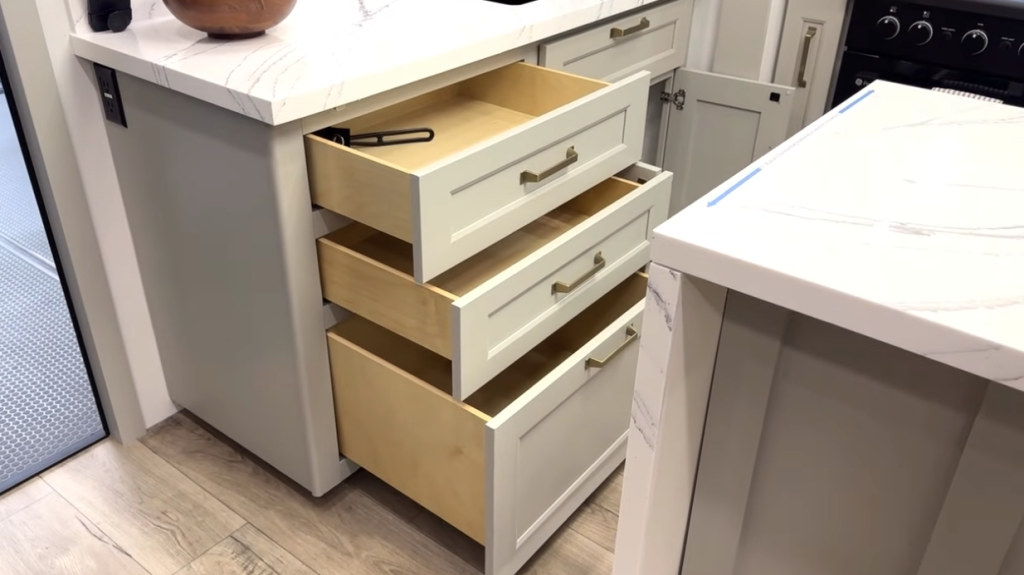 Open kitchen drawers in a modern Brinkley RV showing deep storage space and soft-close cabinetry beneath white marble-style countertops.