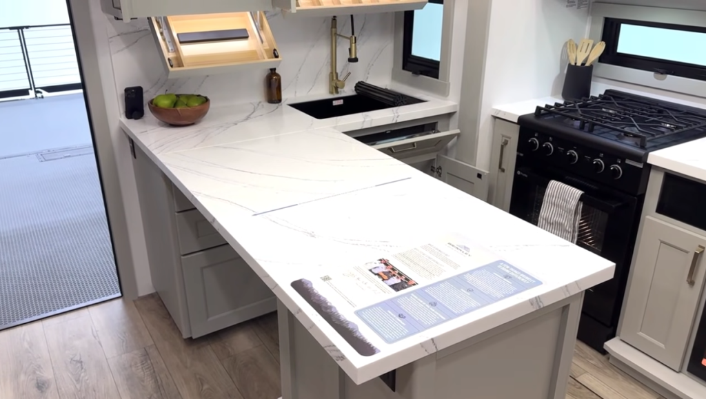 Modern Brinkley RV kitchen with spacious white marble-style countertops, gold faucet, gas cooktop, and light gray cabinetry offering ample prep and storage space.
