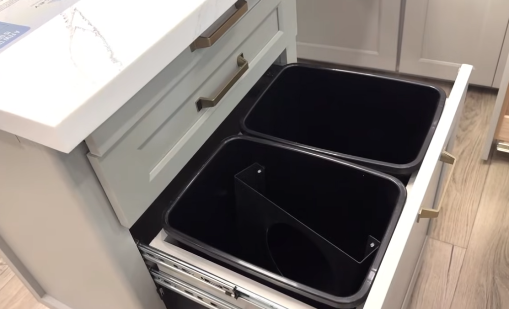 Pull-out dual trash and recycling bins built into the kitchen cabinetry of a modern Brinkley RV for convenient waste separation and storage.