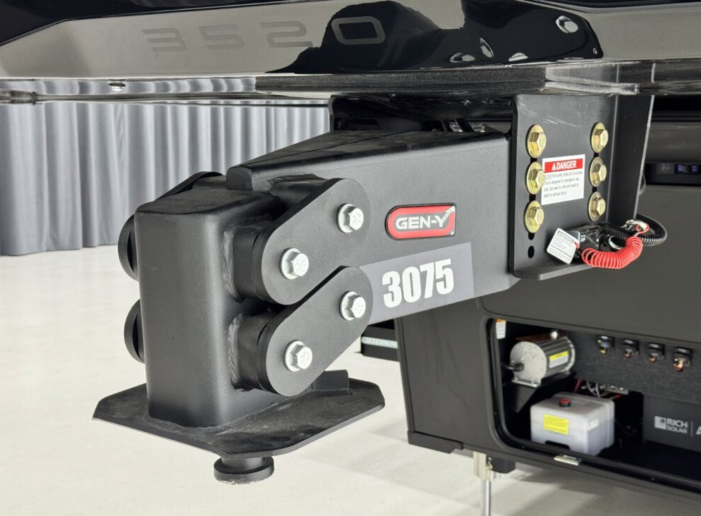 Close-up view of a GEN-Y 3075 fifth-wheel pin box on a Brinkley RV, showing the heavy-duty hitch components, bolts, and electrical breakaway cable for towing stability and safety.