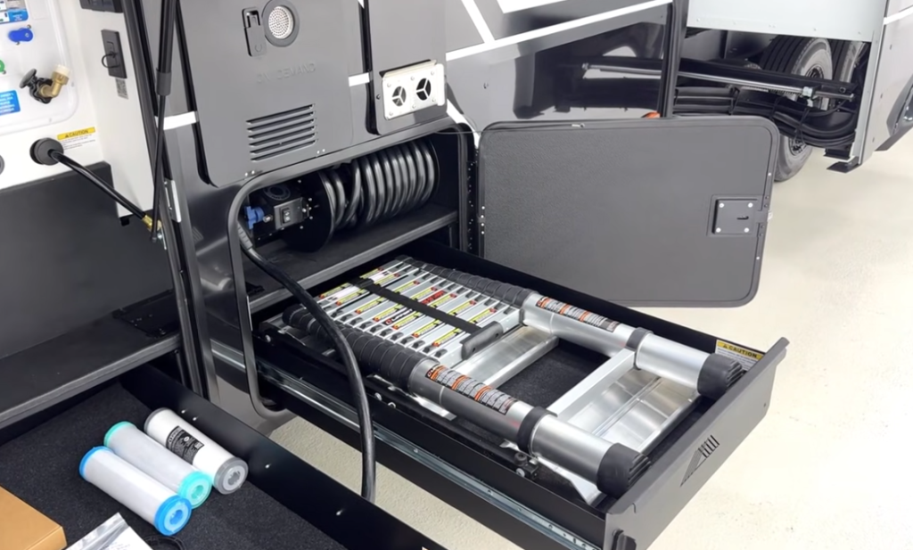 Brinkley fifth wheel pass-through storage showing a slide-out tray with a telescoping ladder, water filtration canisters, and an integrated hose reel in the utility bay.