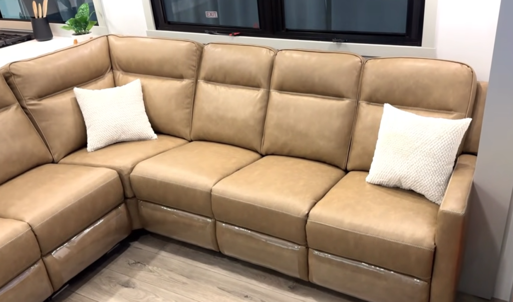Large tan reclining L-shaped sofa in the Brinkley Model Z 3200 fifth wheel, featuring plush cushions, two decorative pillows, and modern RV living room design