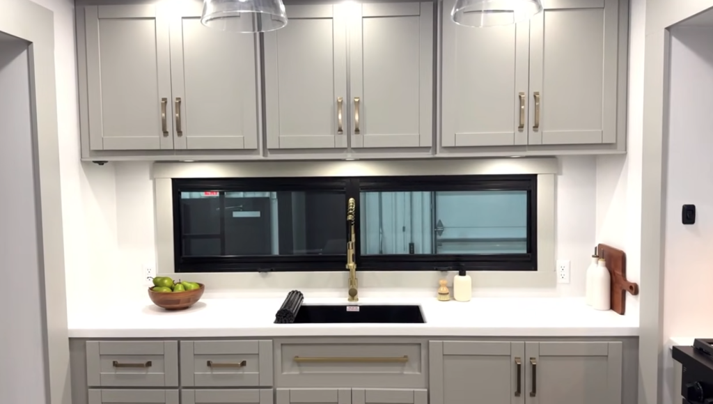 Brinkley Model Z 3200 RV kitchen with modern gray cabinetry, large horizontal window, solid-surface countertops, farmhouse-style sink with gold faucet, and residential-inspired storage.