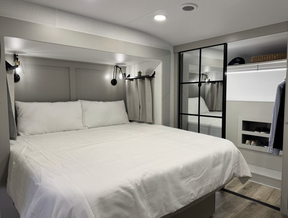 Brinkley Model Z 3200 bedroom with king bed, modern reading lights, overhead storage shelf with curtains, and large mirrored wardrobe closet showcasing spacious RV bedroom design.