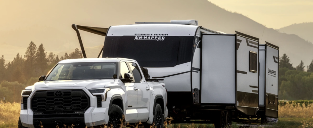 Toyota Tundra towing a Forest River Un-Mapped travel trailer with slide-outs extended in a scenic mountain meadow at sunset.
