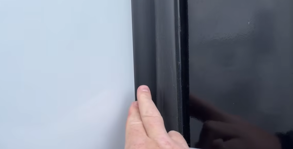 Close-up of RV exterior trim and seal with a finger pointing at the rubber gasket, illustrating proper RV seal inspection and maintenance.