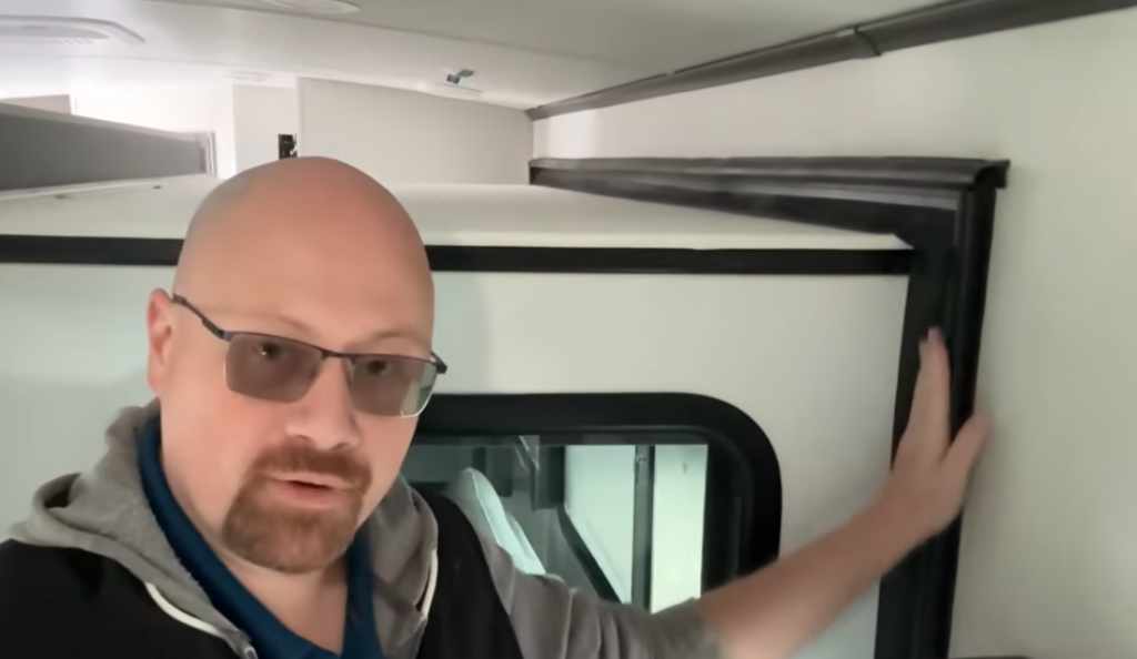 Man pointing out RV interior wall trim and seal near a window, explaining proper RV maintenance and care to prevent damage and wear.