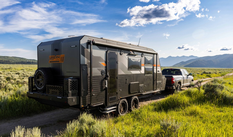 Off-road travel trailer being towed through open grassland and mountains, showcasing rugged adventure-ready RV camping.