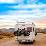 Motorhome driving down a desert road at sunset with bicycles mounted on the rear rack, highlighting adventure travel and RV road trip lifestyle.