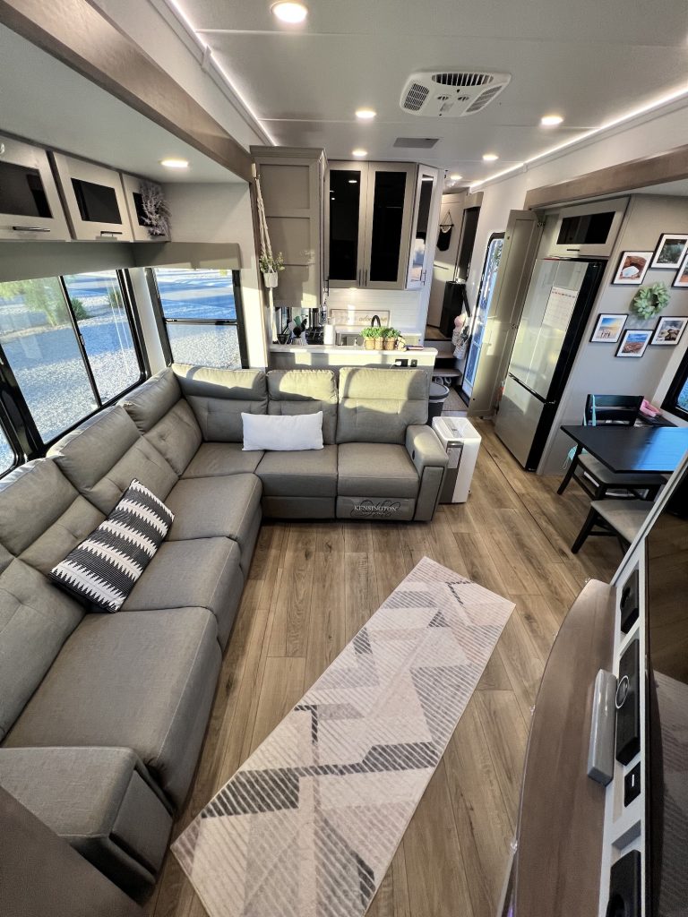 RV living room wide angle shot with an L-shaped couch, dining area and view of the kitchen.