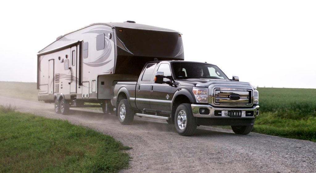 Heavy-duty pickup truck towing a fifth wheel RV on a rural gravel road, demonstrating real-world fifth wheel towing stability, truck capability, and off-highway RV travel conditions.
