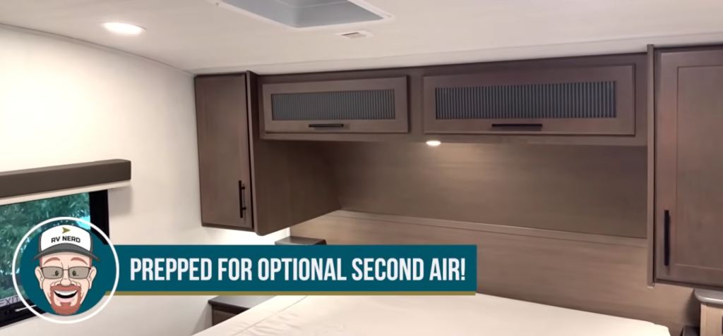 RV bedroom overhead cabinets above the bed with integrated lighting and ceiling vent, showing factory prep for an optional second air conditioner, highlighting expanded climate control capability in a modern RV sleeping area.