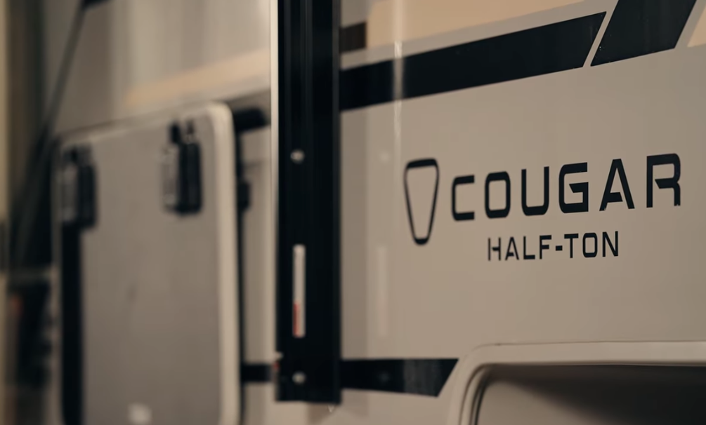Close-up exterior view of a Cougar Half-Ton travel trailer logo and sidewall branding, highlighting lightweight RV design and half-ton towability.