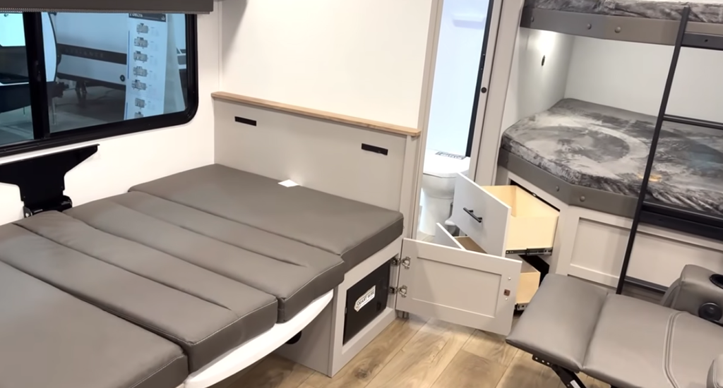 RV bunkhouse with fold-down sofa bed, hidden storage drawers, and stacked bunk beds with ladder, showing flexible sleeping and storage space in a family-friendly travel trailer interior.