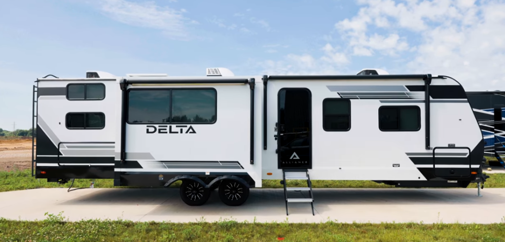 Side profile of Alliance Delta travel trailer with dual axles, large slide-out, exterior entry steps, modern black-and-white graphics, and tinted windows parked outdoors under a blue sky.
