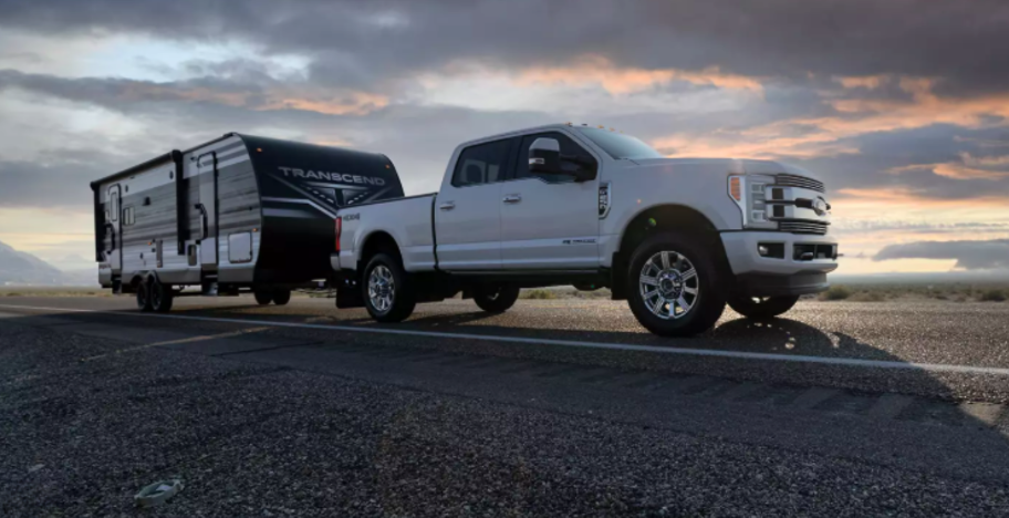 Pickup truck towing a Transcend travel trailer on an open highway at sunset