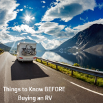 RV driving along a scenic mountain road beside a lake, representing things to know before buying an RV