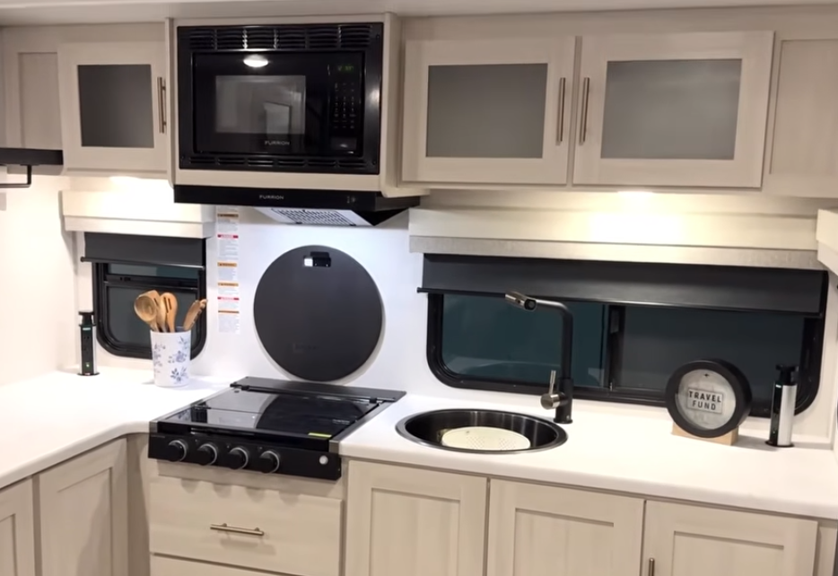 RV kitchen with microwave, three-burner stove, round sink, and overhead cabinets