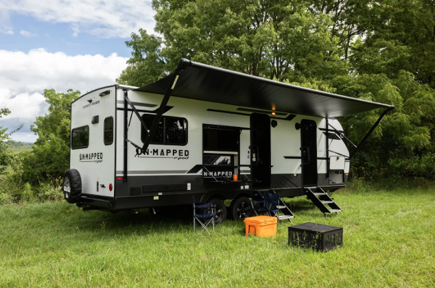Forest River Unmapped travel trailer set up at campsite with large awning, chairs, and outdoor gear