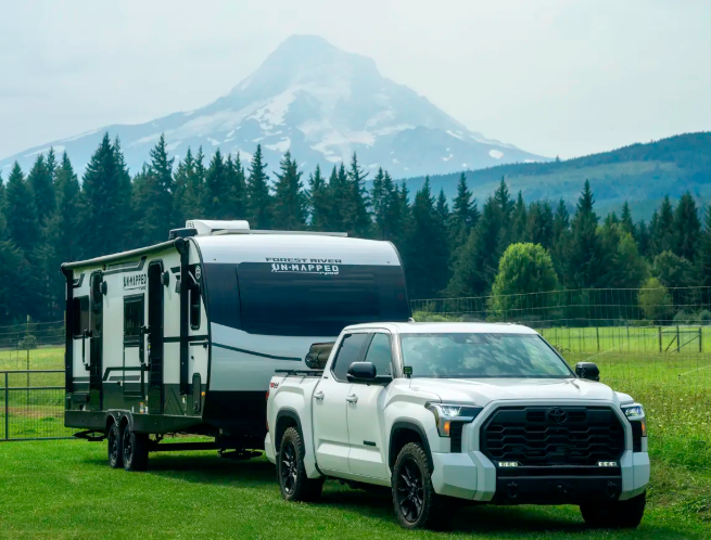 Travel trailer being towed by pickup truck in mountain landscape with forest and snowcapped peak