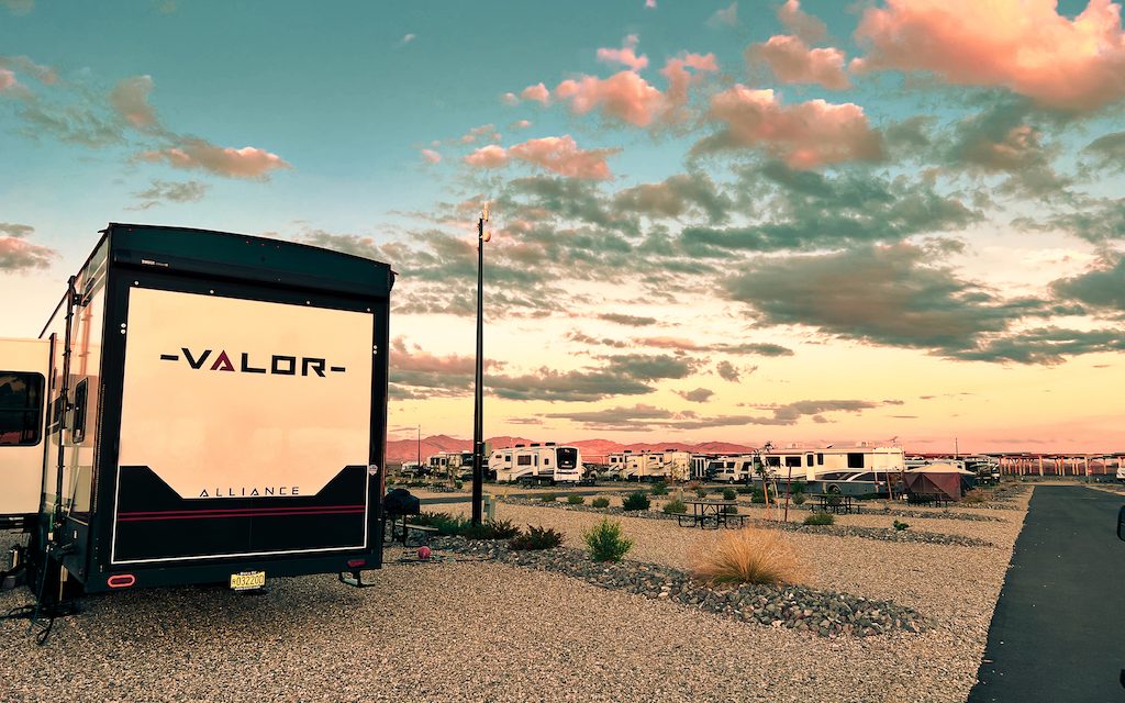 RV parked at a desert RV resort campground at sunset with mountains and multiple RV sites in the background