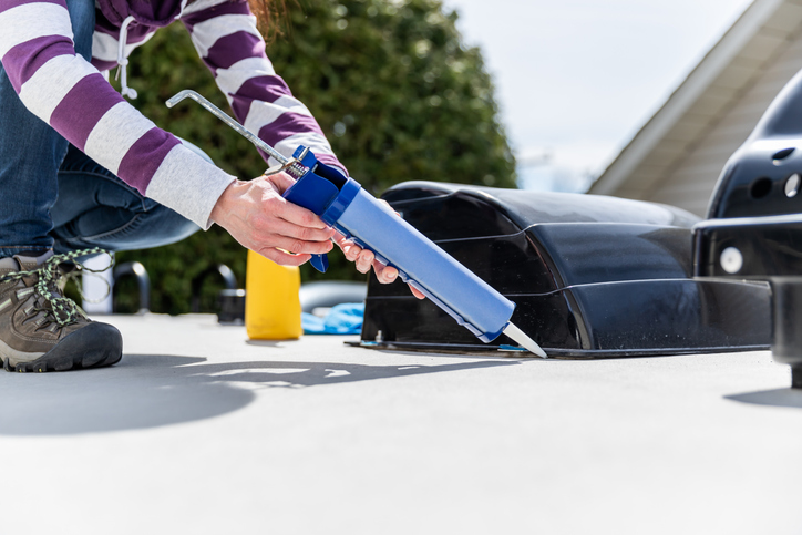 A woman is doing the maintenance of a camper trailer. She is applying a sealant around the windows and other parts of the trailer. The seasonal maintenance of a travel trailer, a caravan, a motor home or a camper trailer is very important to enjoy the camping season.
