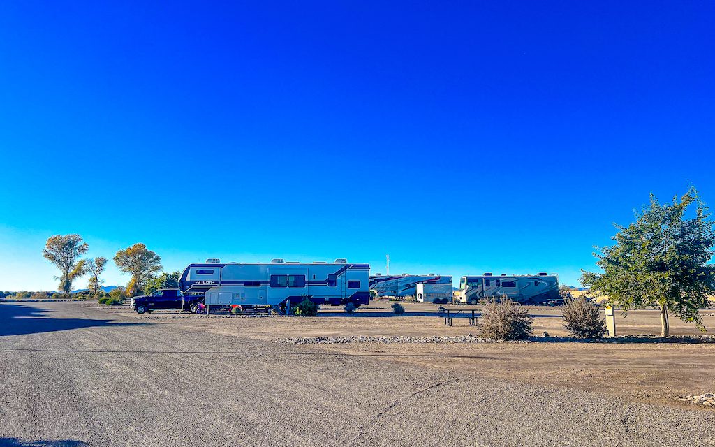 RVs parked at a spacious desert campground under a clear blue sky with picnic tables and open sites