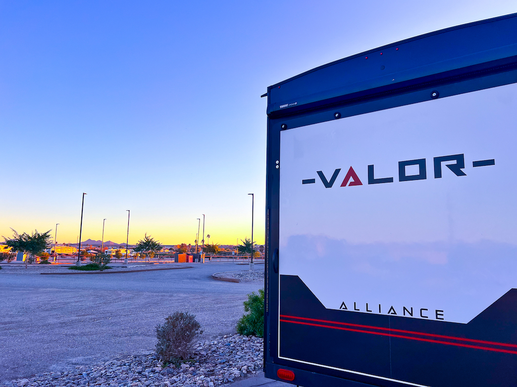 Alliance Valor fifth wheel RV parked at a desert RV resort during sunset with open sites and mountain views