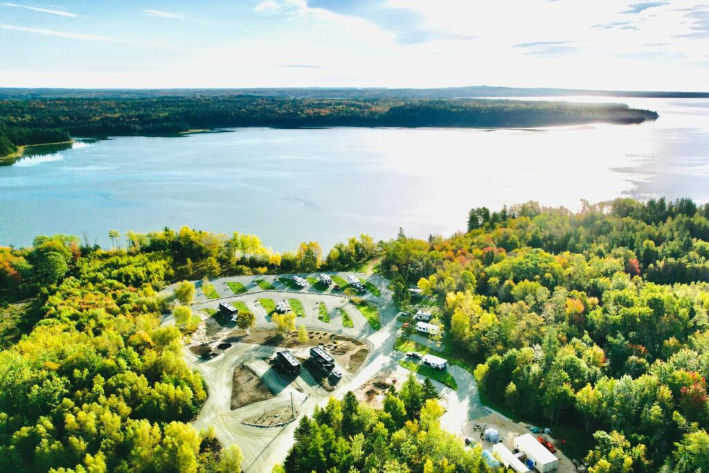 Aerial view of a lakeside RV campground surrounded by colorful fall foliage, with full-hookup campsites nestled among dense forest overlooking a scenic waterfront.