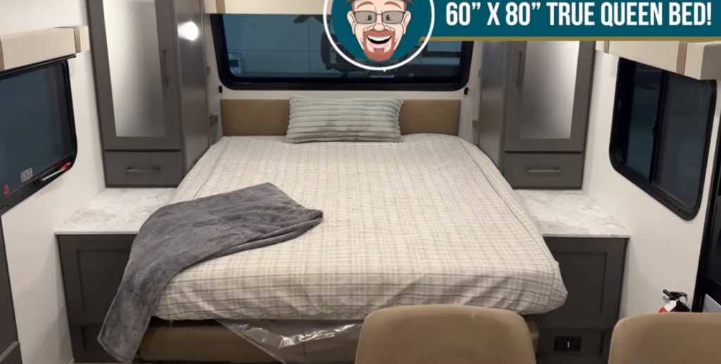 True queen bed setup inside travel trailer with side wardrobes, nightstands, and rear window