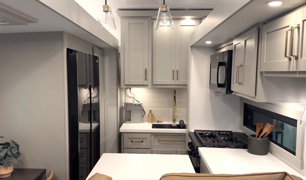 Luxury RV kitchen with residential refrigerator, gas range, microwave, and shaker cabinets