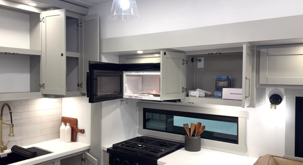 RV kitchen with open overhead cabinets and built-in microwave above gas range